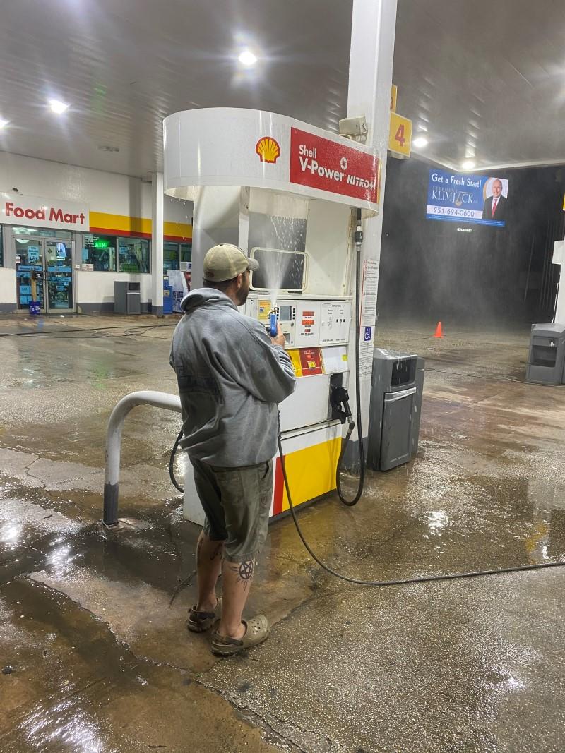Technician pressure washing a gas station fuel pump island at night.