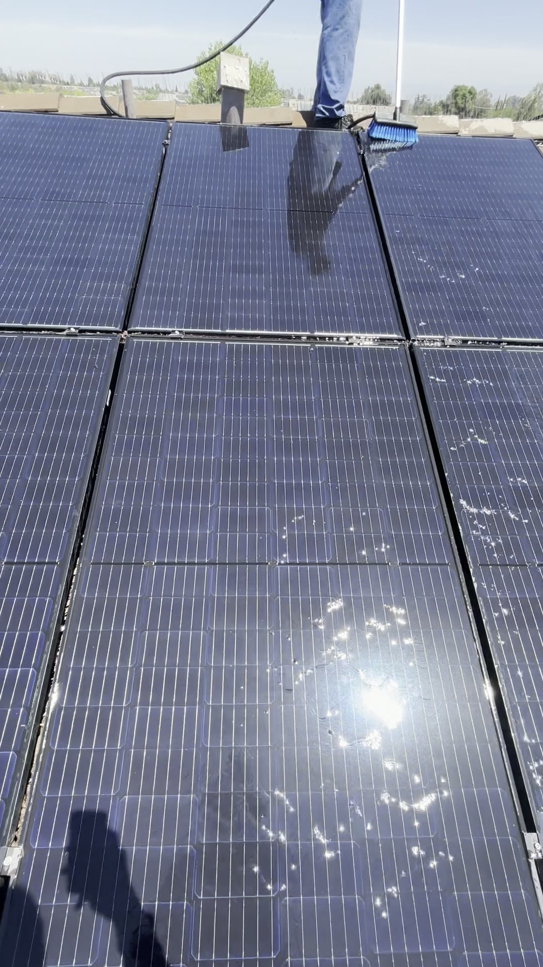 Technician squeegeeing water across a rooftop solar array mid-clean under a clear sky.