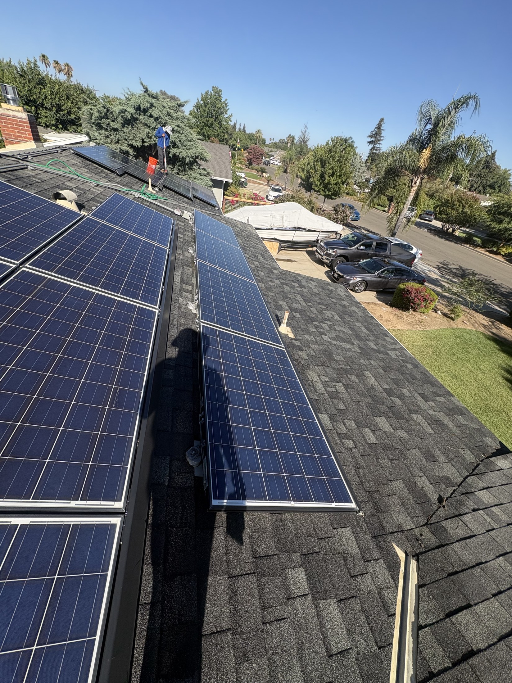 Technician cleaning a rooftop solar array during the day over a residential neighborhood.