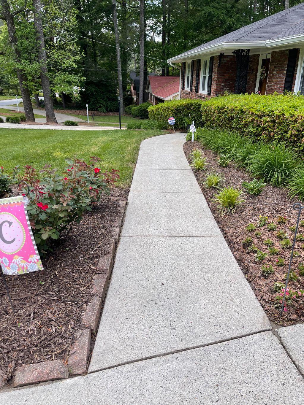 Clean residential walkway leading to a brick home with tidy landscaping.
