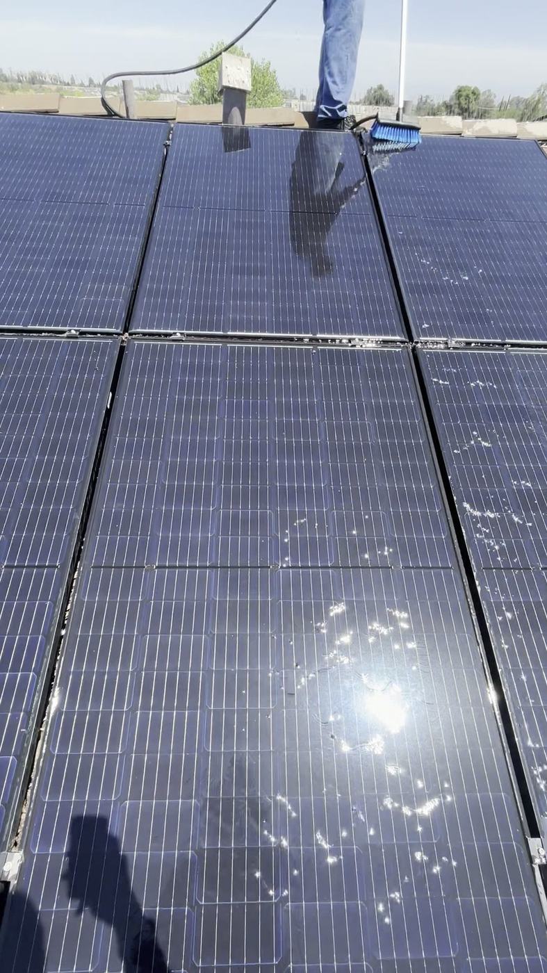 Technician squeegeeing water across a rooftop solar array mid-clean under a clear sky.